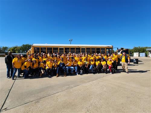 large group of adults in gold shirts in front of school bus